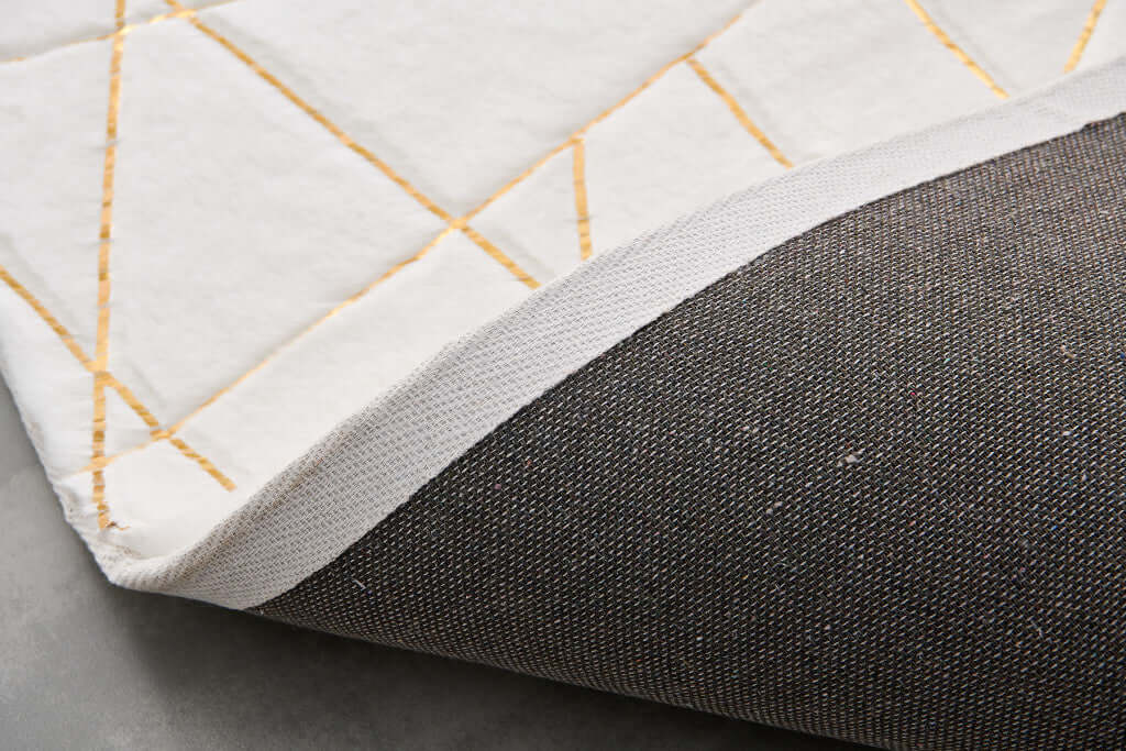 Close-up of the backing of a white and gold faux fur area rug showing non-skid design and abstract pattern.