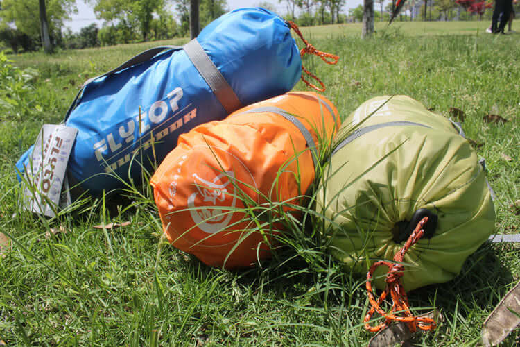 Colorful camping tent bags in green, orange, and blue, placed on grass in an outdoor setting.