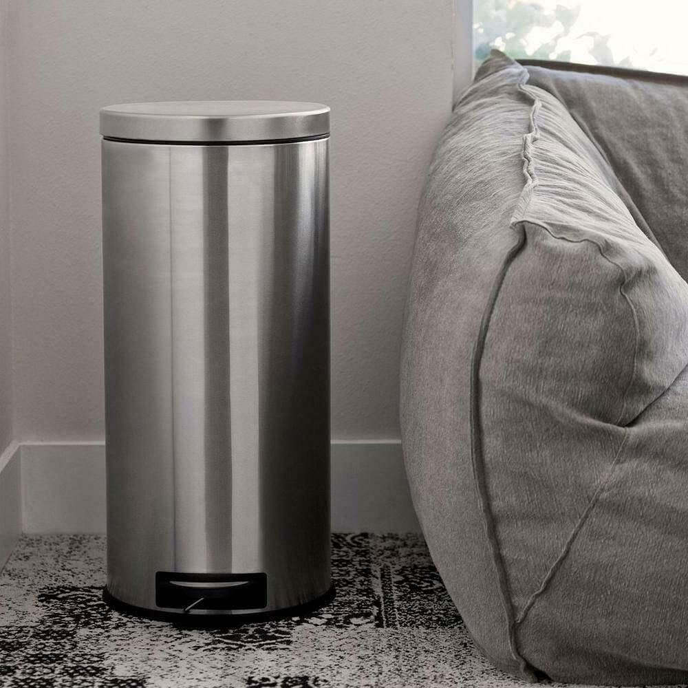 8-gallon round stainless steel step trash can next to a gray couch in a modern living space.