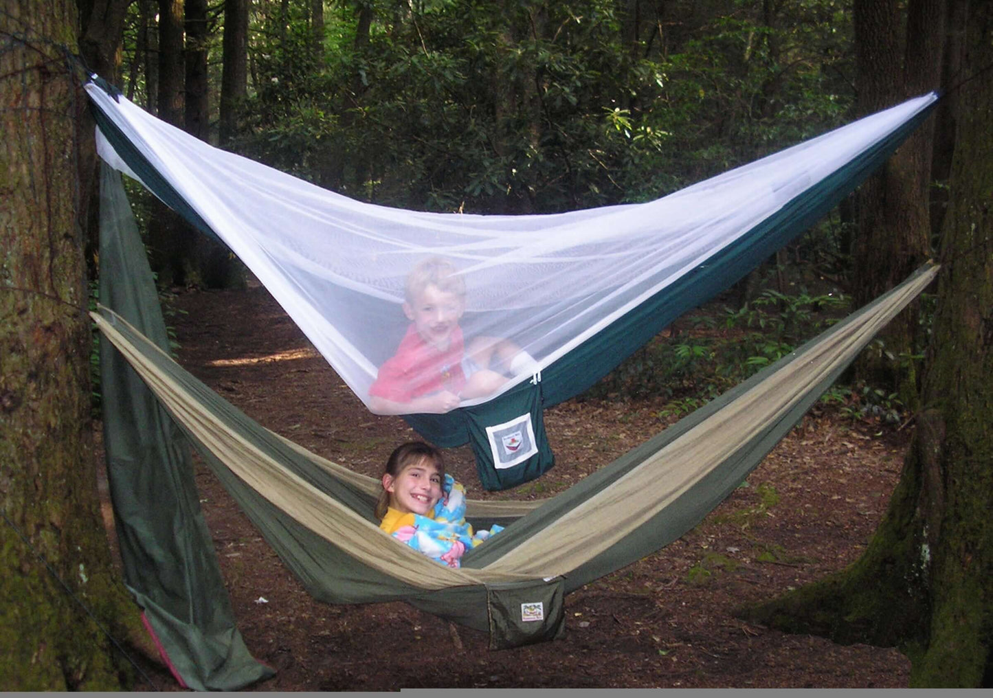 Two children enjoying a spacious Mosquito Free Hammock with white mosquito netting in a forest setting.